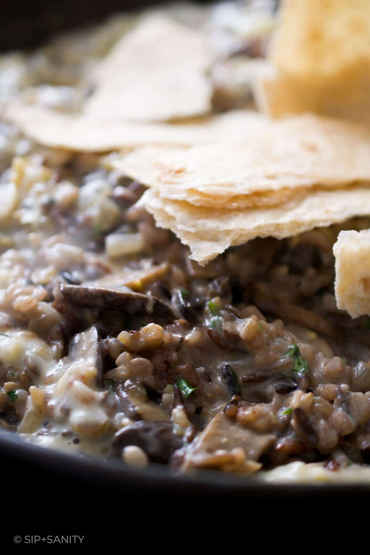 Torn whole wheat tortillas being added to a skillet of rice and mushrooms.