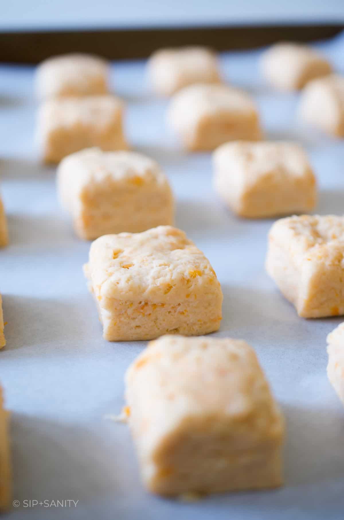 Prebaked square biscuits on a parchment lined sheet pan.