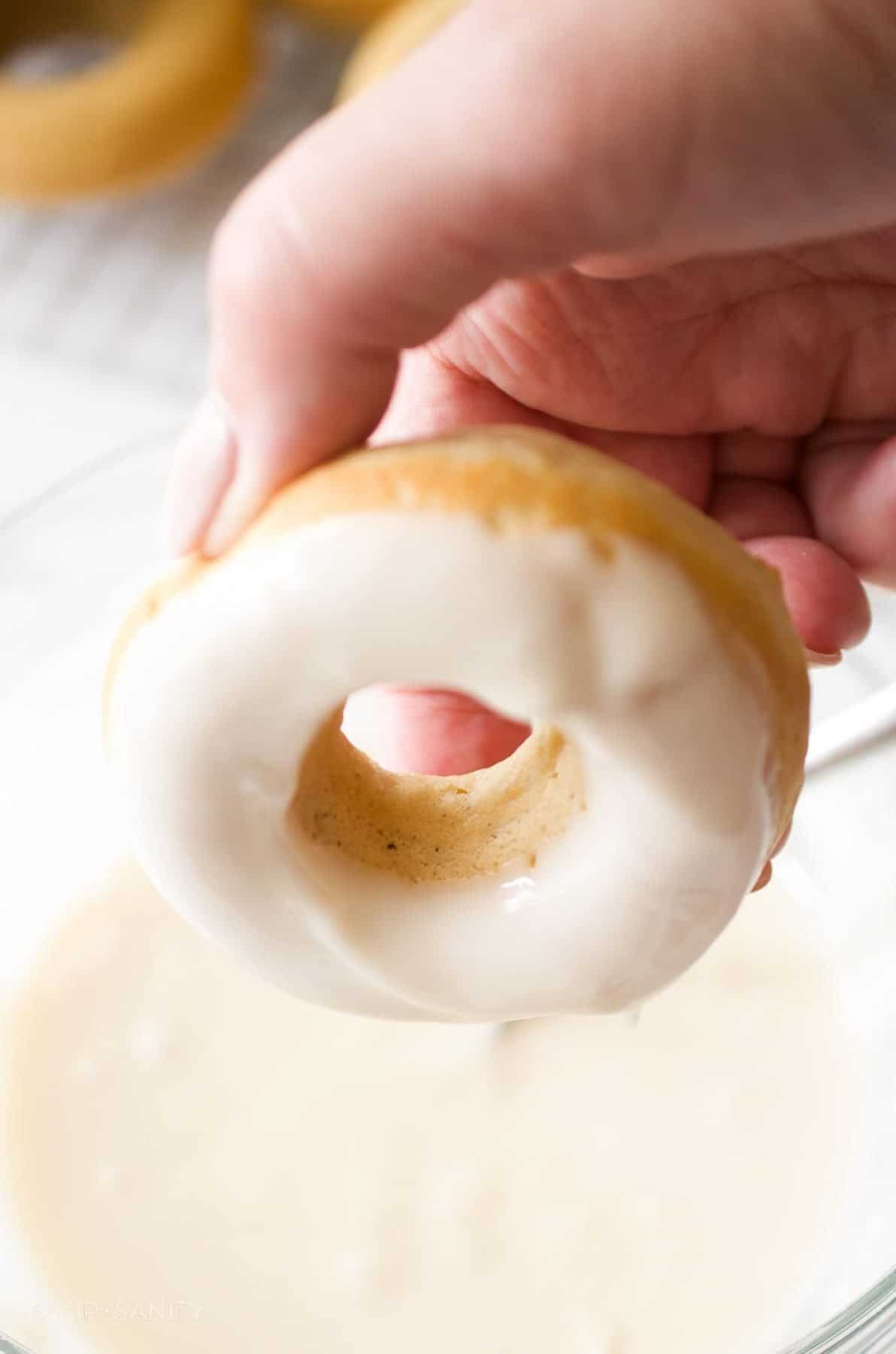 Dipping baked donuts into a bowl of glaze.