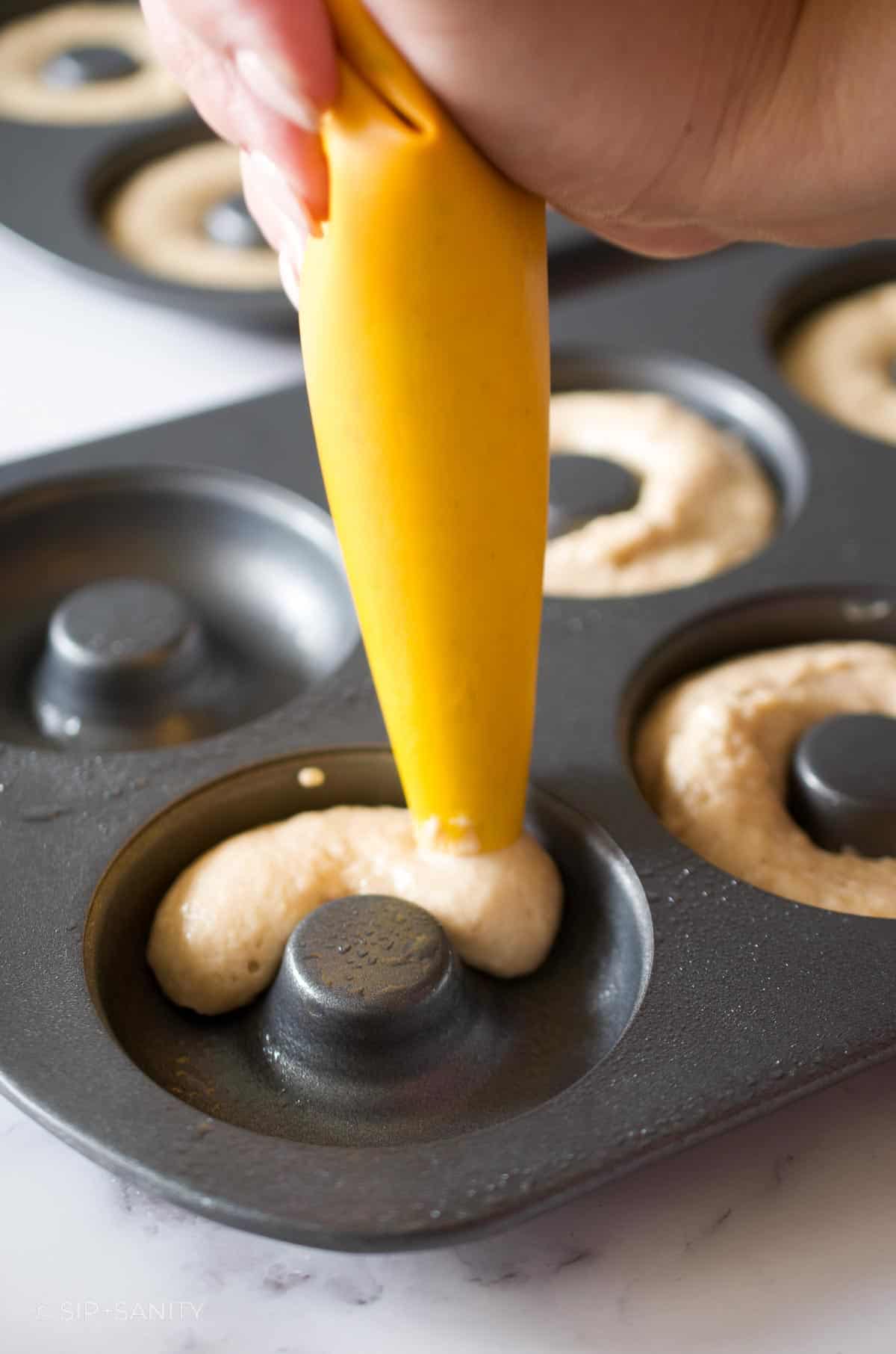 Piping donut batter into a baked donut pan.