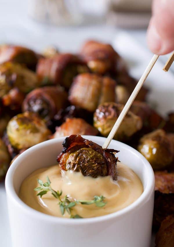 Dipping a bacon wrapped brussels sprouts into a bowl of maple mustard.