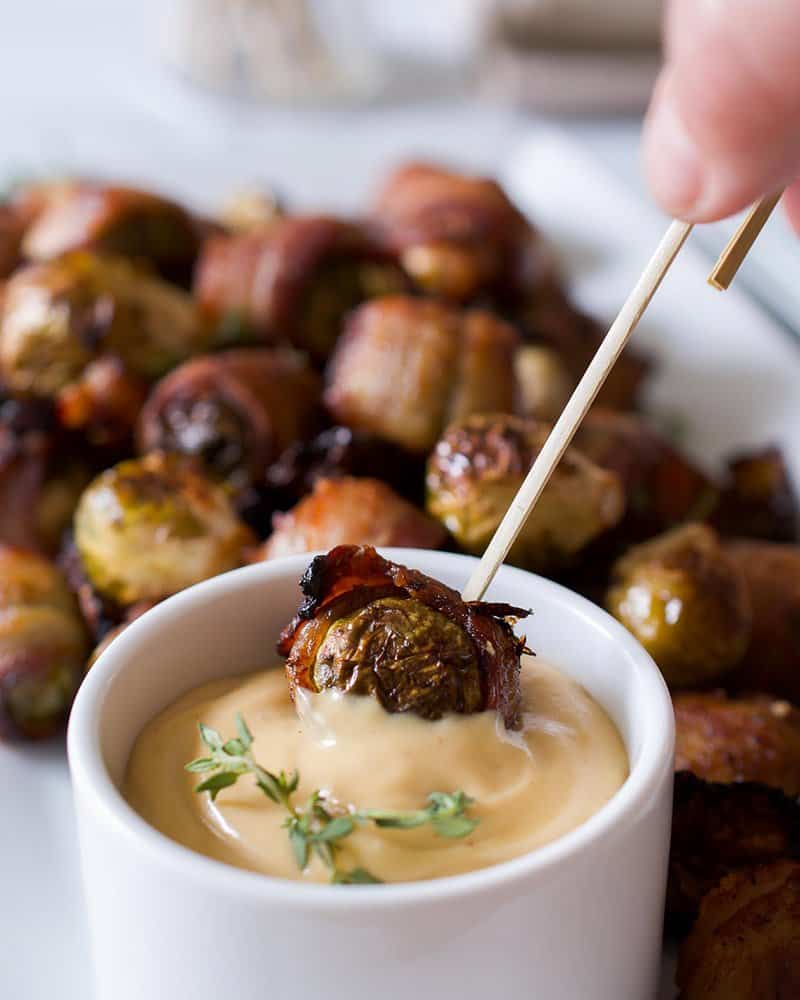 Dipping a bacon wrapped brussels sprouts into a bowl of maple mustard.