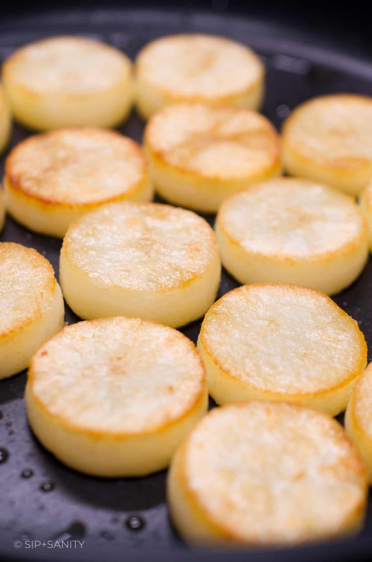Circles of russet potatoes sautéing in a nonstick skillet.