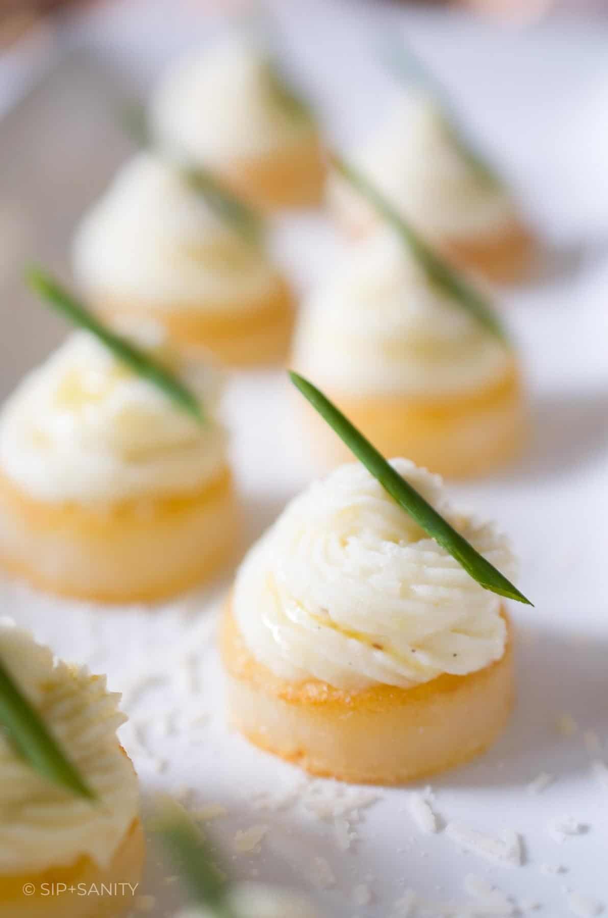 Round potato appetizers garnished with a chive sprig on a white dish.