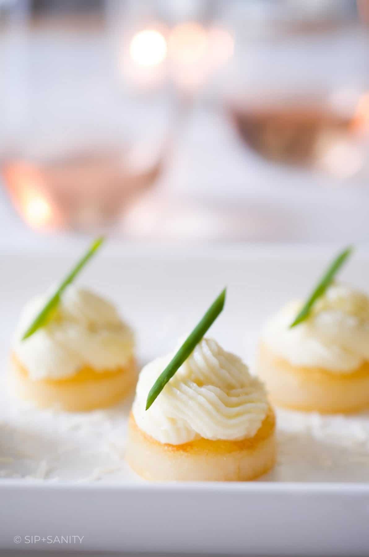 A trio of potato appetizers in front of two glasses of rose wine.