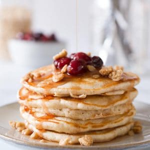 Stack of pancakes topped with cranberry maple syrup and oat crumble.