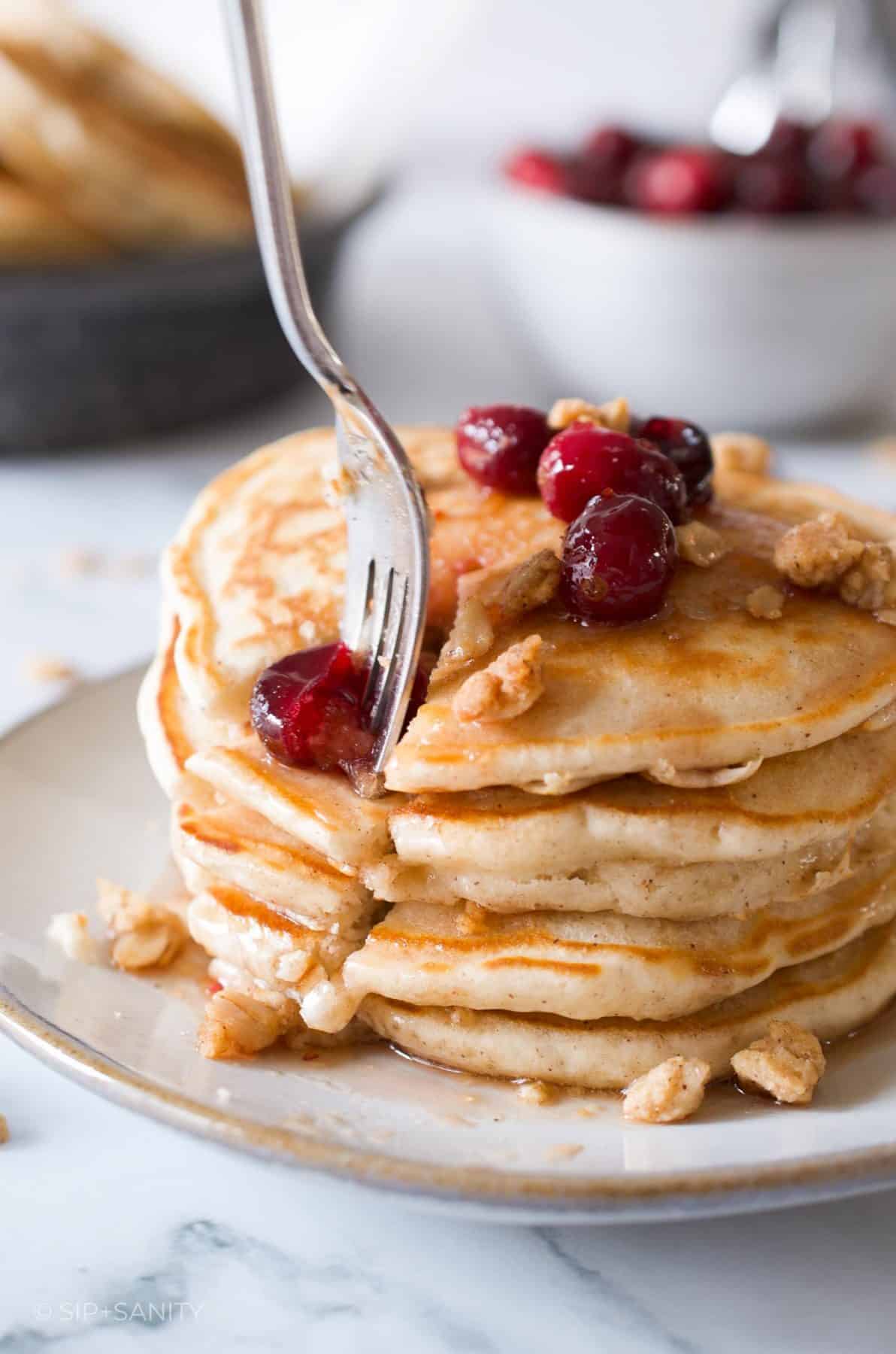 A fork spearing a wedge of pancakes topped with cranberry maple syrup and oat crumble.