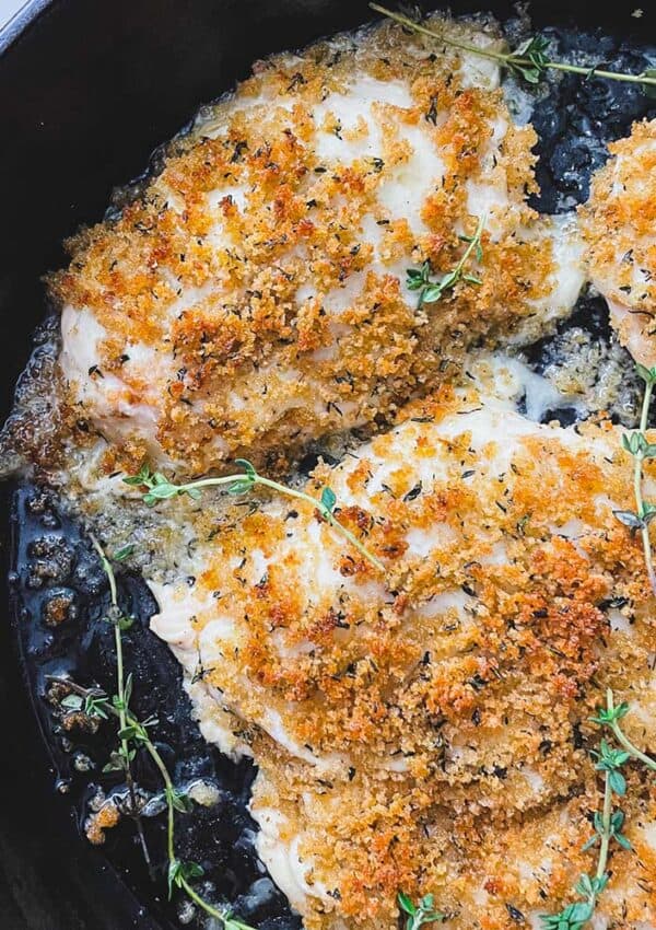 Breadcrumb topped roasted chicken breasts with thyme in a cast iron skillet.