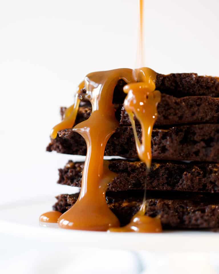 A stack of brownie brittle pieces with caramel sauce dripping down.