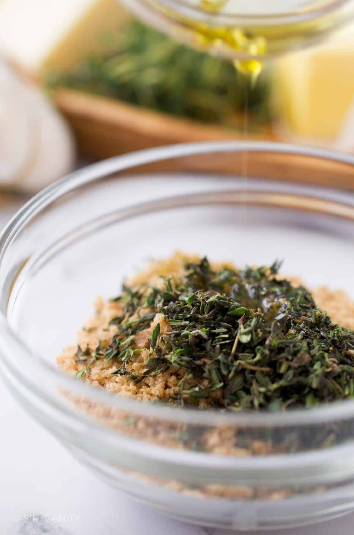 Fresh thyme and breadcrumbs in a bowl with olive oil being drizzled over.