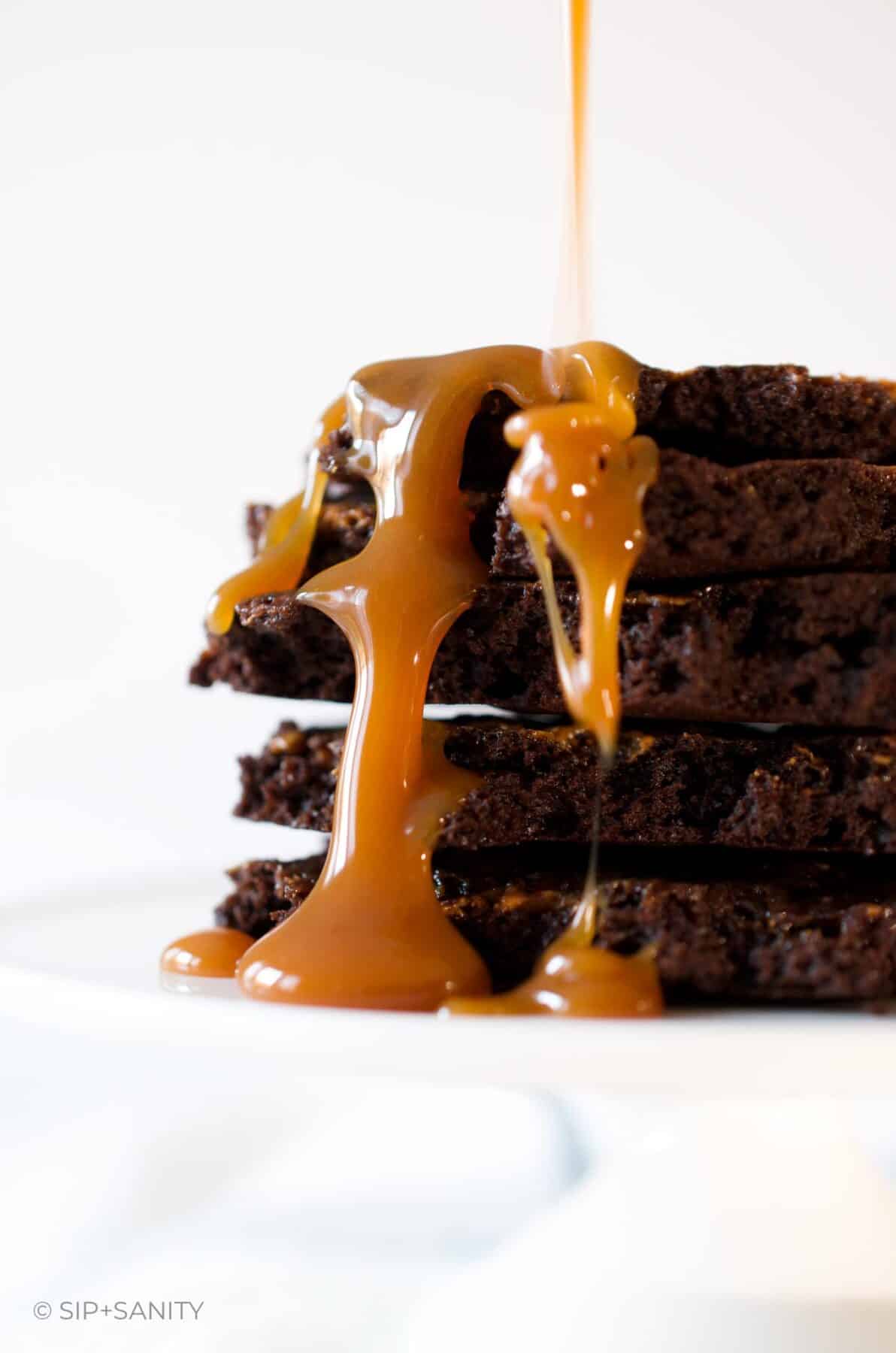 A stack of brownie brittle pieces with caramel sauce dripping down.