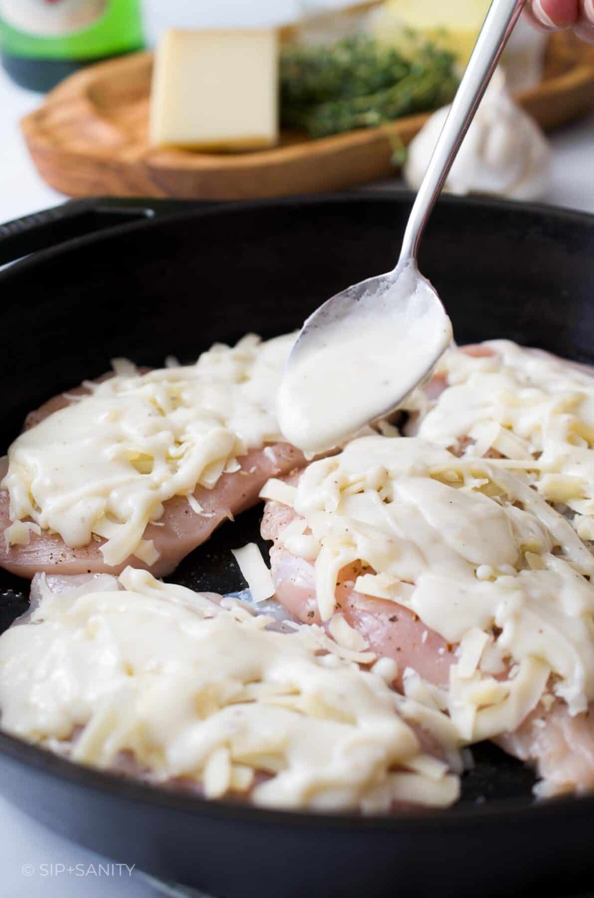 Spooning a creamy sauce over cheese topped chicken breasts.