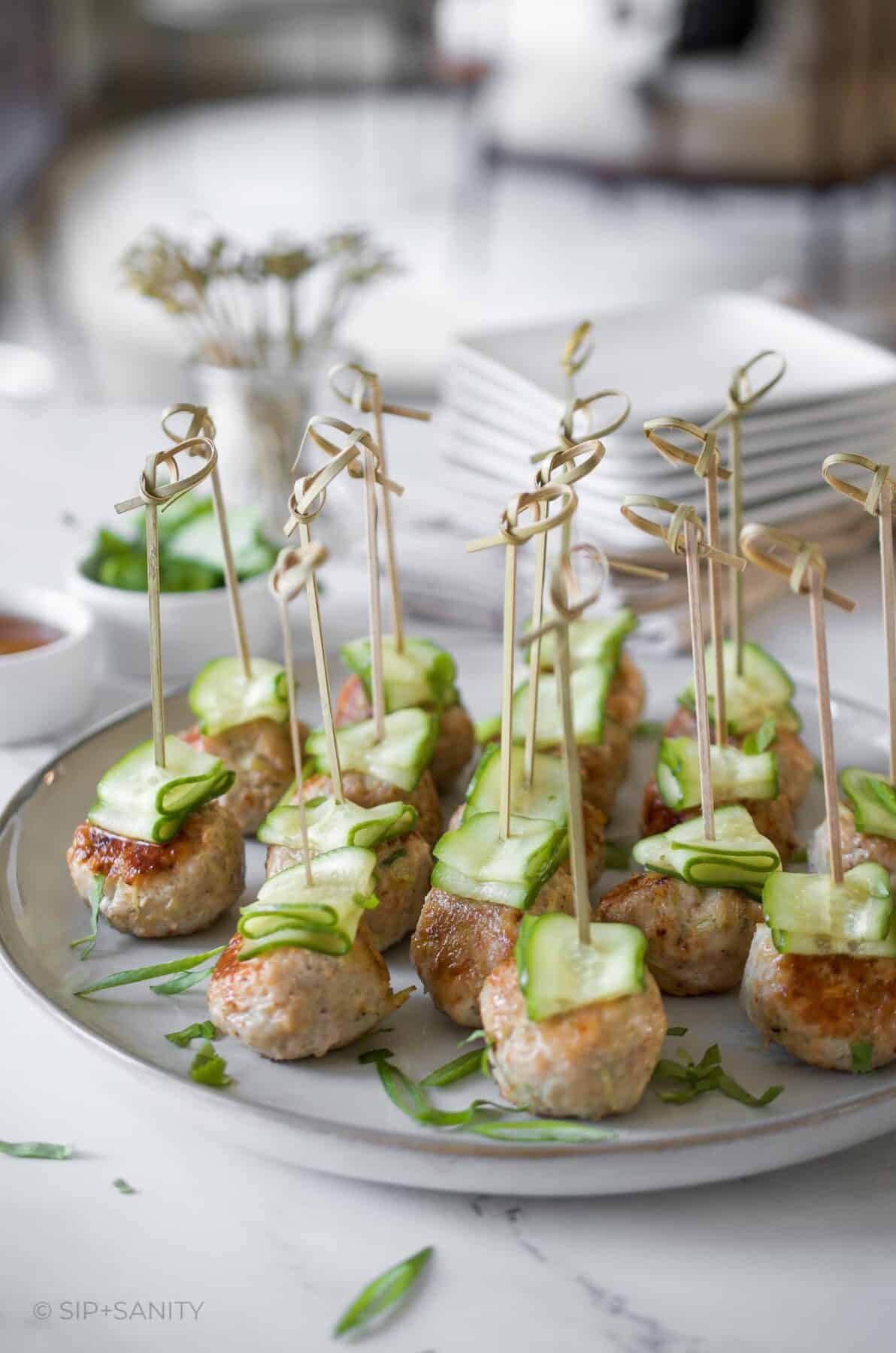 A platter of asian style meatballs topped with cucumber ribbons on cocktail picks.