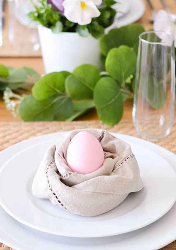 A pink egg nestled in a napkin that looks like a nest on a spring dining table.