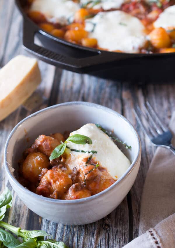 A small bowl of gnocchi with tomato sauce and mozzarella next to a cast iron skillet filled with more gnocchi.