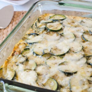 A green glass casserole dish with zucchini rounds and melted cheese on a placemat.