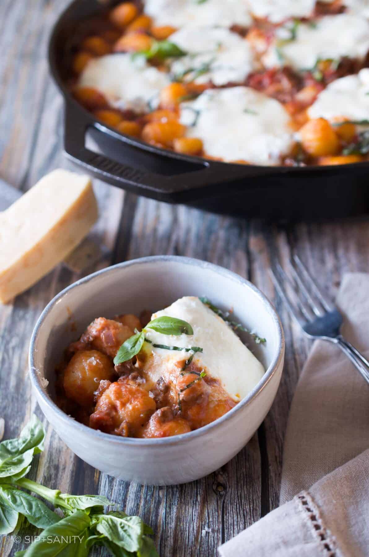 A small bowl of gnocchi with tomato sauce and mozzarella next to a cast iron skillet filled with more gnocchi.