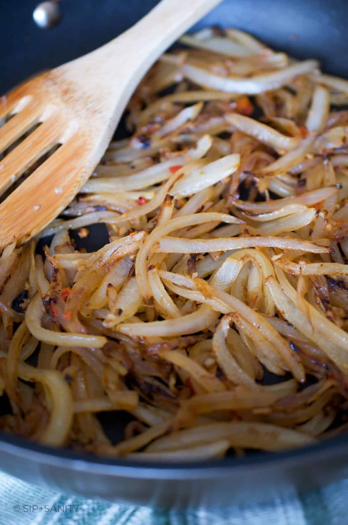 Caramelized strips of onion in a skillet with a wooden spoon resting on the edge.