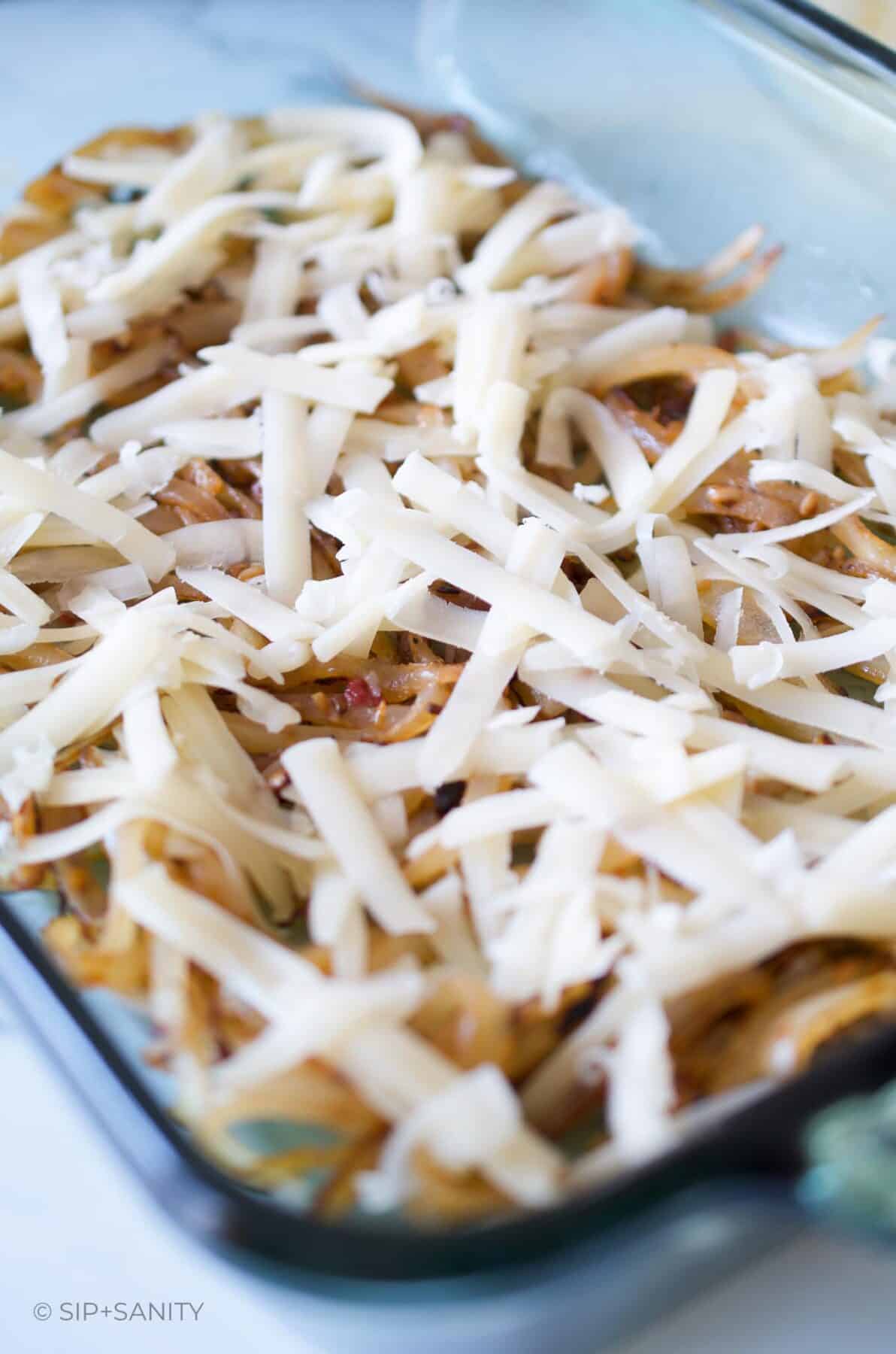 A green glass casserole dish with caramelized onions and shredded white cheese in it.