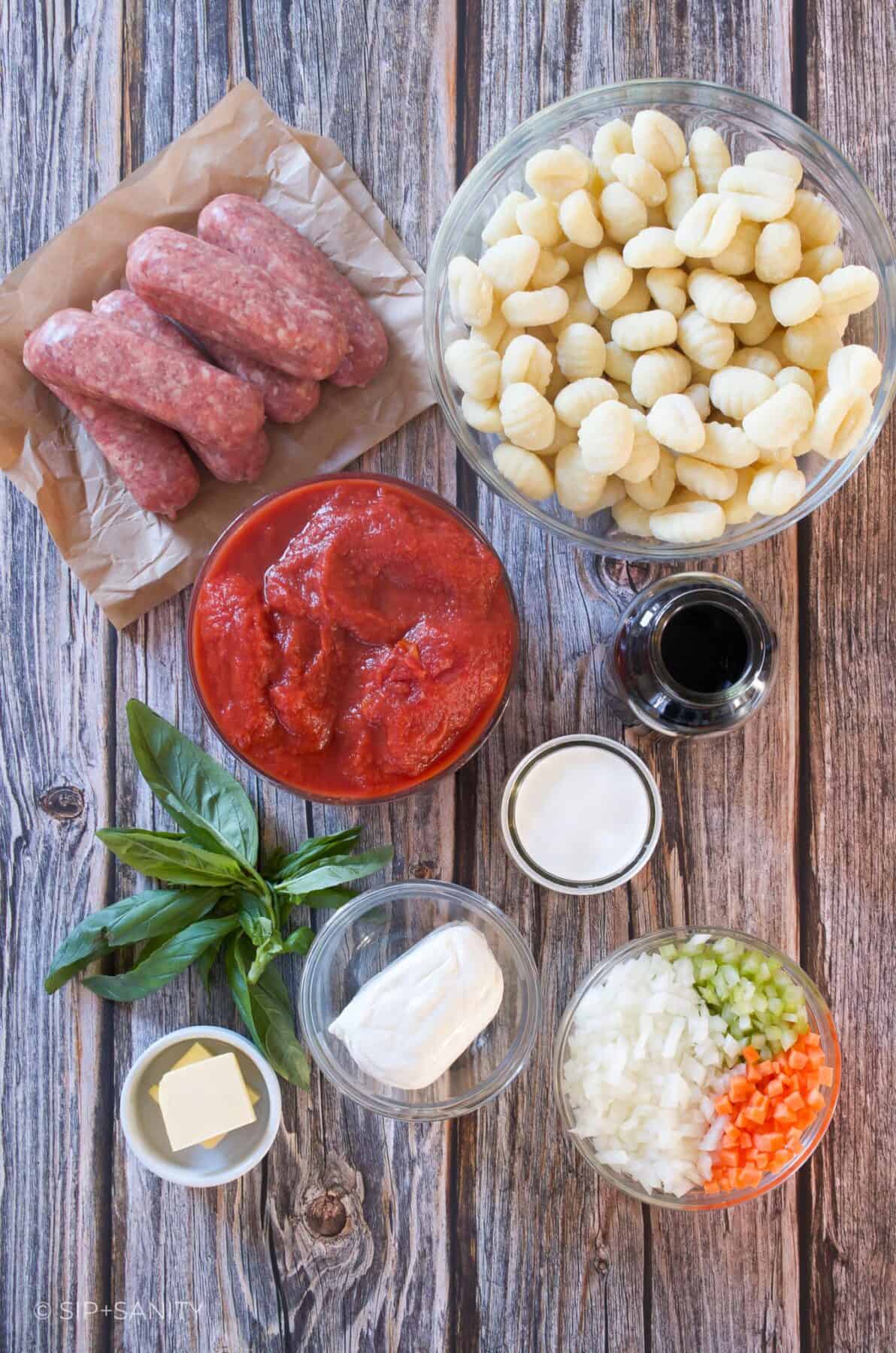 Raw ingredients for baked gnocchi and sausage ragu on a wooden table.