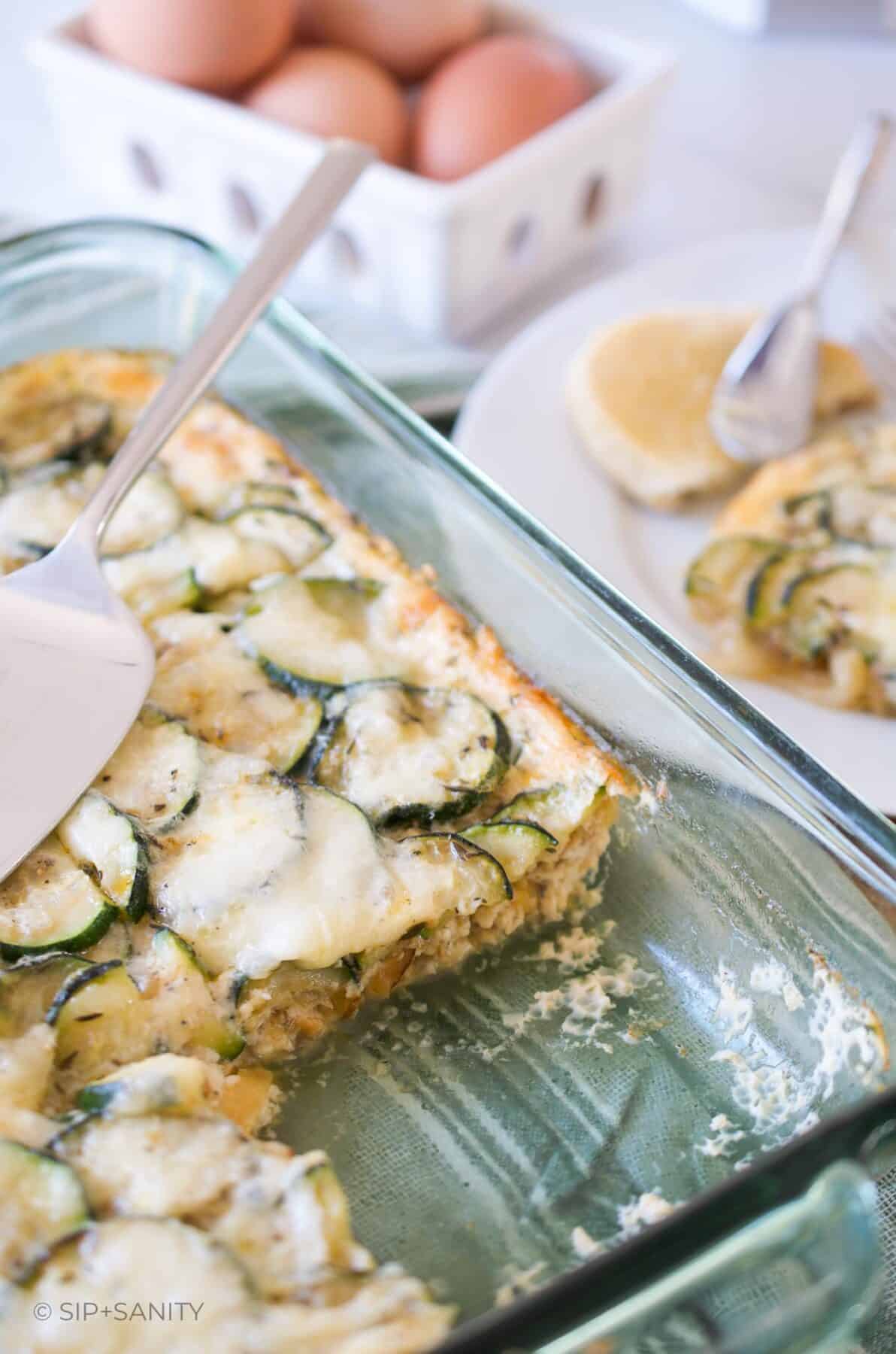 A green glass casserole dish with zucchini rounds and melted cheese with a slice missing.