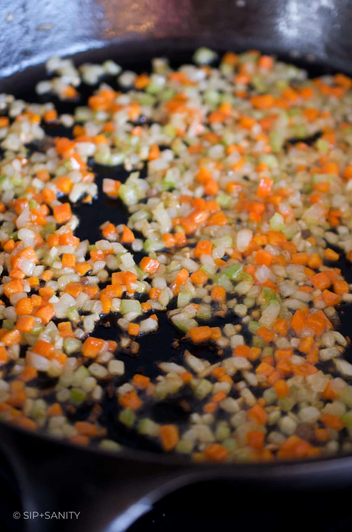 Diced carrots, celery and onion sautéing in butter in a cast iron skillet.