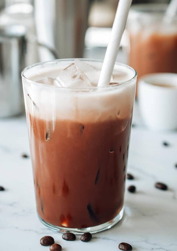 A glass filled chocolate shaken espresso topped with a layer of frothy almond milk on a white table.