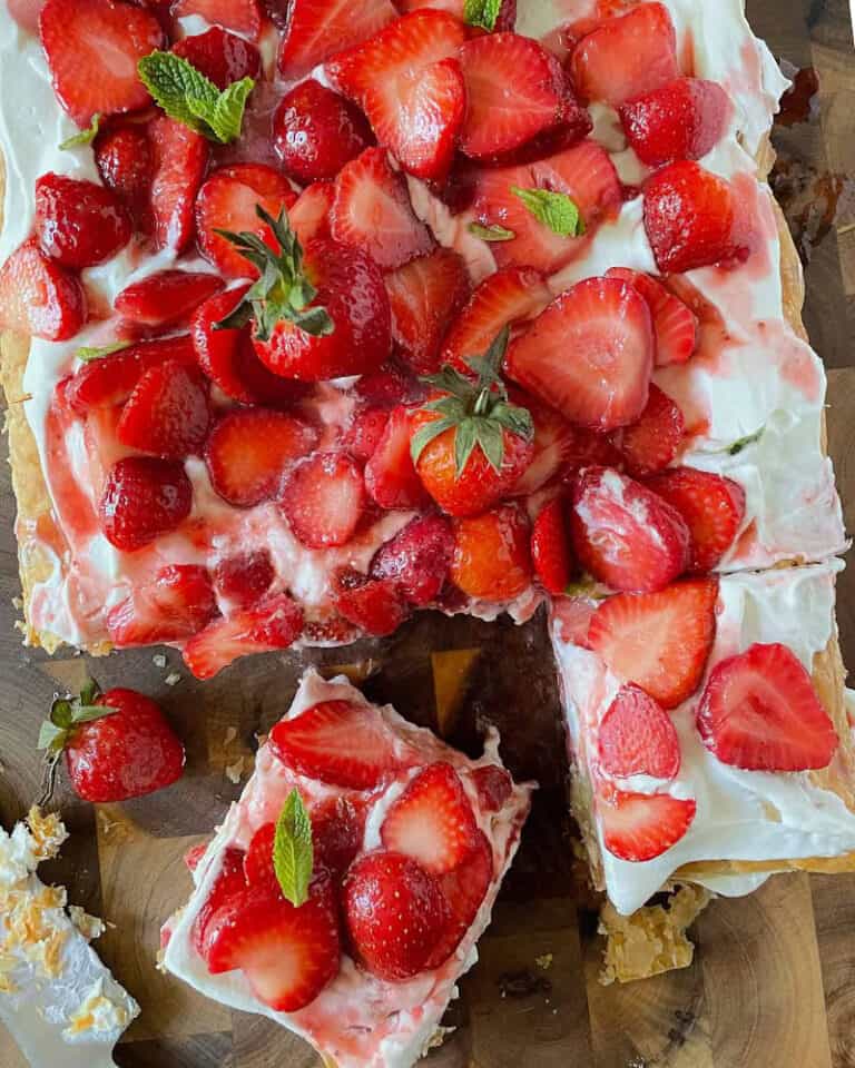 A giant strawberry shortcake dessert made with puff pastry on a cutting board.