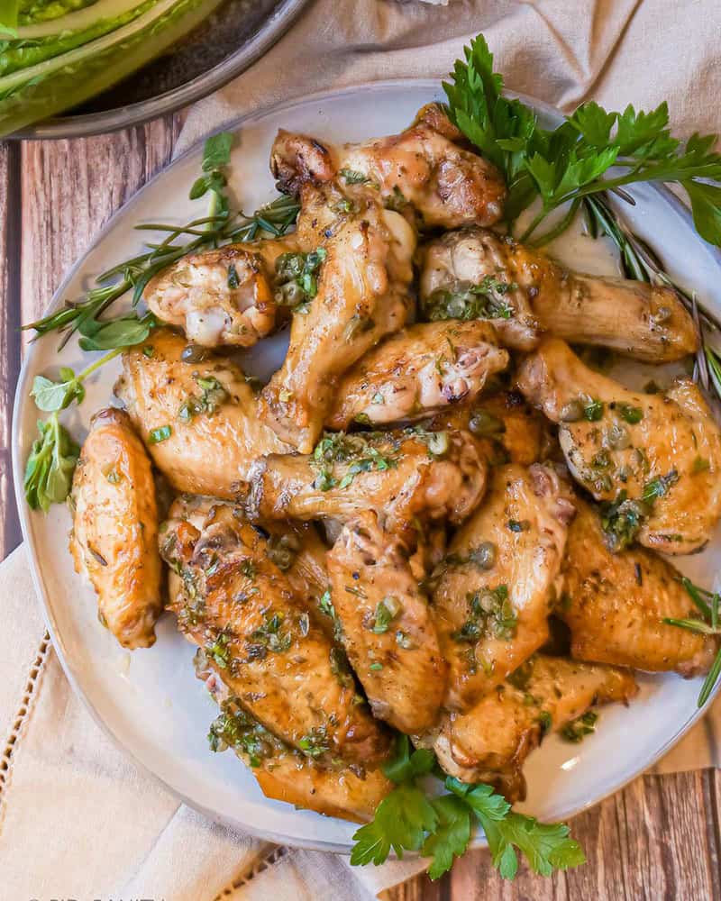 A platter of grilled italian chicken wings garnished with herbs and lemon dressing.