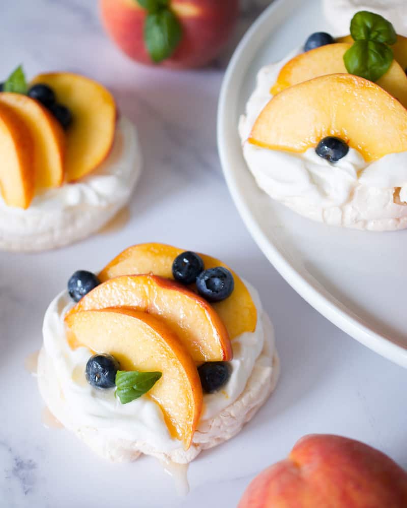 Miniature pavlovas topped with fresh sliced peaches, blueberries and basil.
