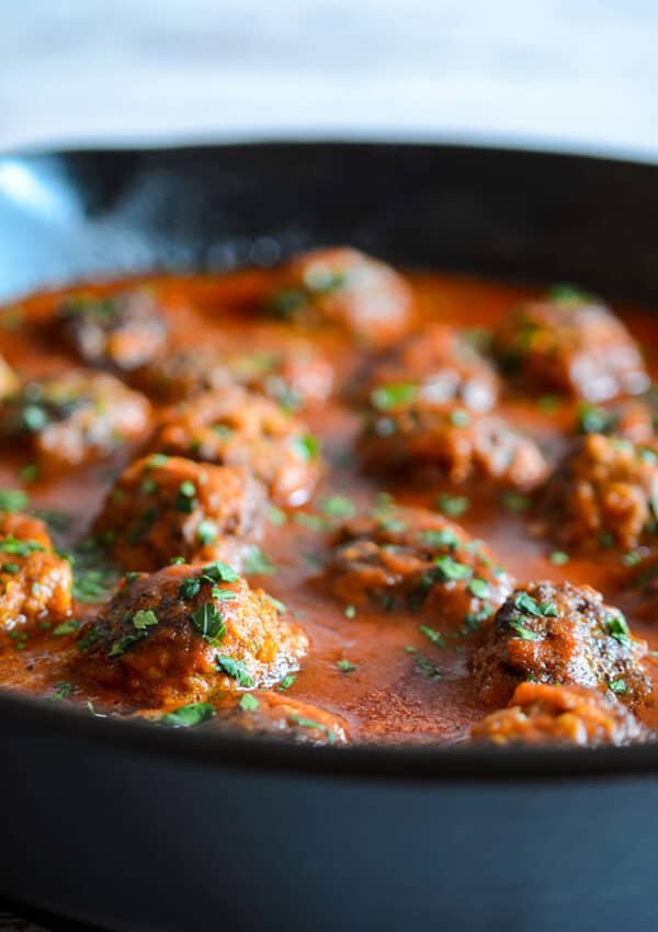 Juicy meatballs swimming in tomato sauce in a cast iron skillet garnished with parsley.