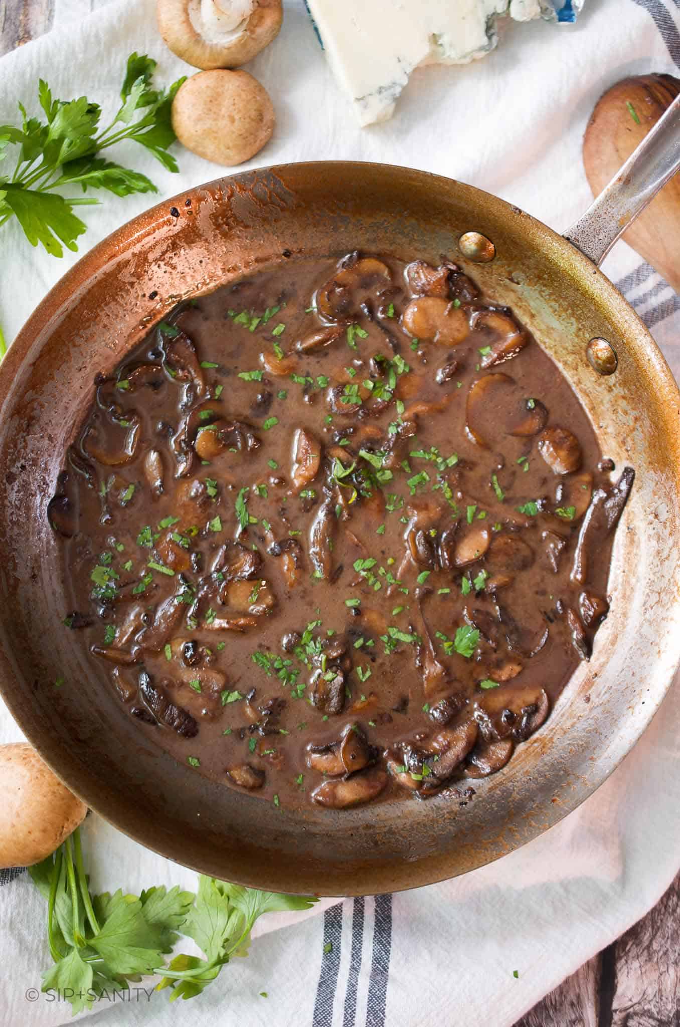 Overhead photo of a saute pan filled with mushroom marsala sauce next to mushrooms and a block of gorgonzola.