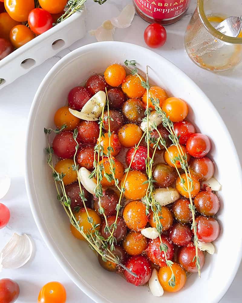 Oval casserole filled with multi-colored cherry tomatoes, sprigs of thyme and garlic cloves.