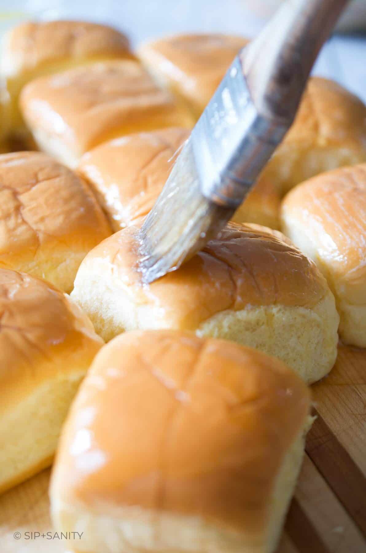 Potato dinner rolls being brushed with melted butter.