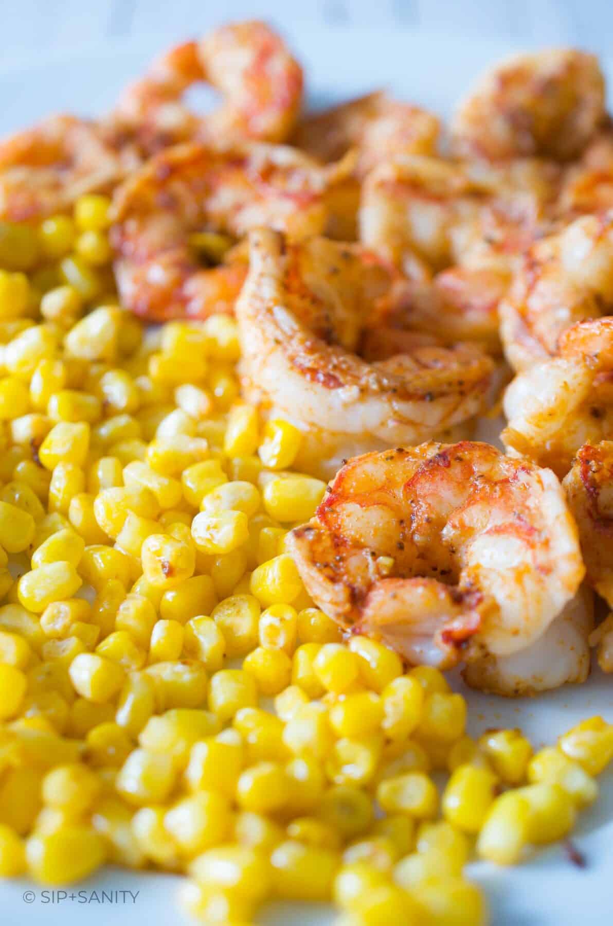 Sauteed shrimp and corn kernels cooling on a plate.