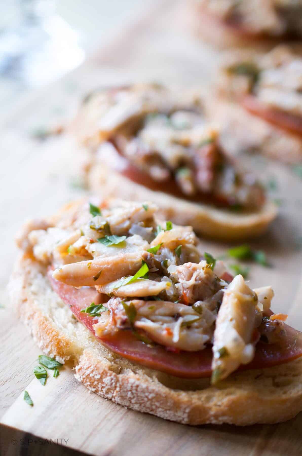 Servings of spicy warm crab bruschetta on a wood serving tray.
