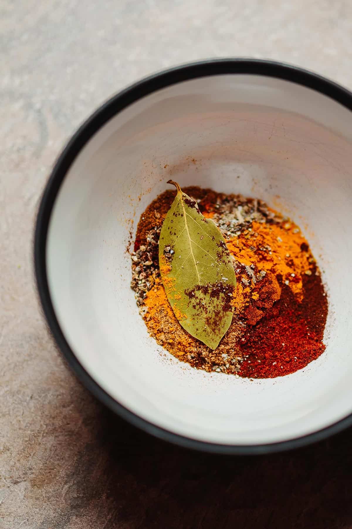 A small ceramic bowl filled with spices and a bay leaf, Photo by Andy Holmes on Unsplash.