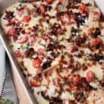 A casserole topped with melted cheese, bacon bits and halved cherry tomatoes.