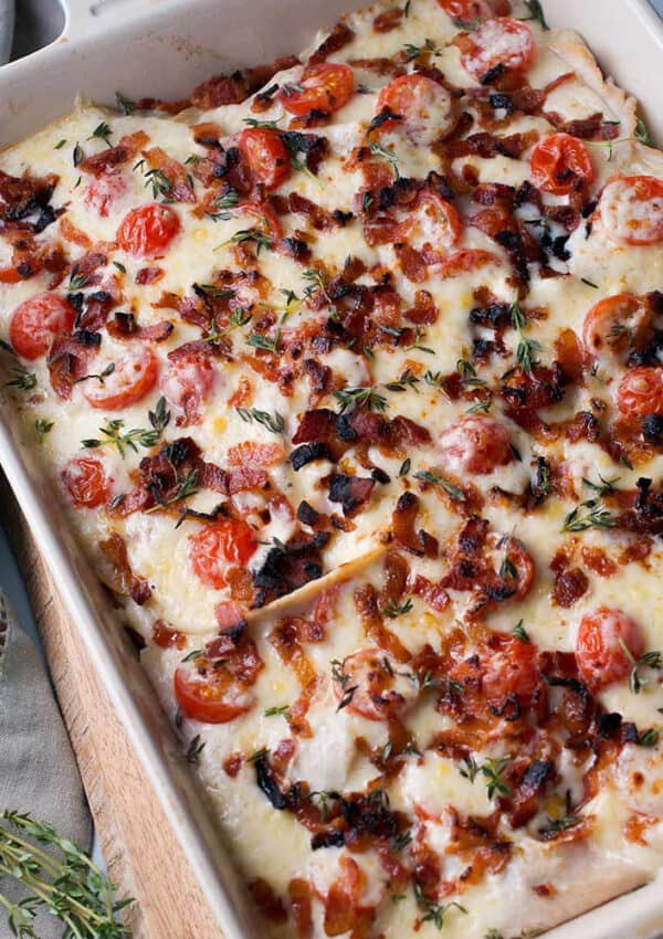 A casserole topped with melted cheese, bacon bits and halved cherry tomatoes.
