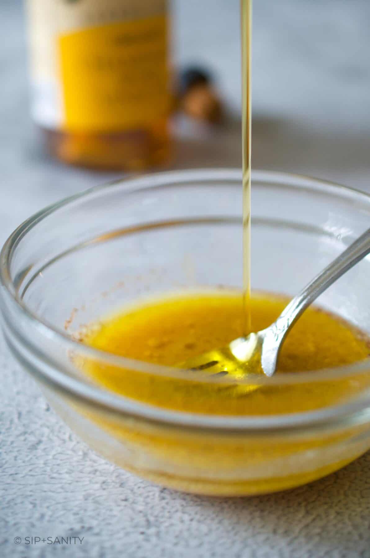 Olive oil being drizzled into a bowl with vinegar and mustard.