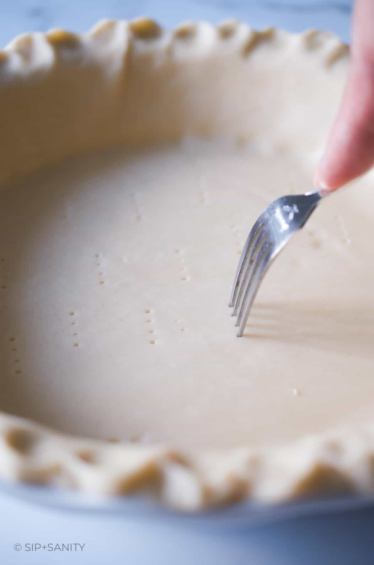 Pricking an unbaked pie shell with a fork.