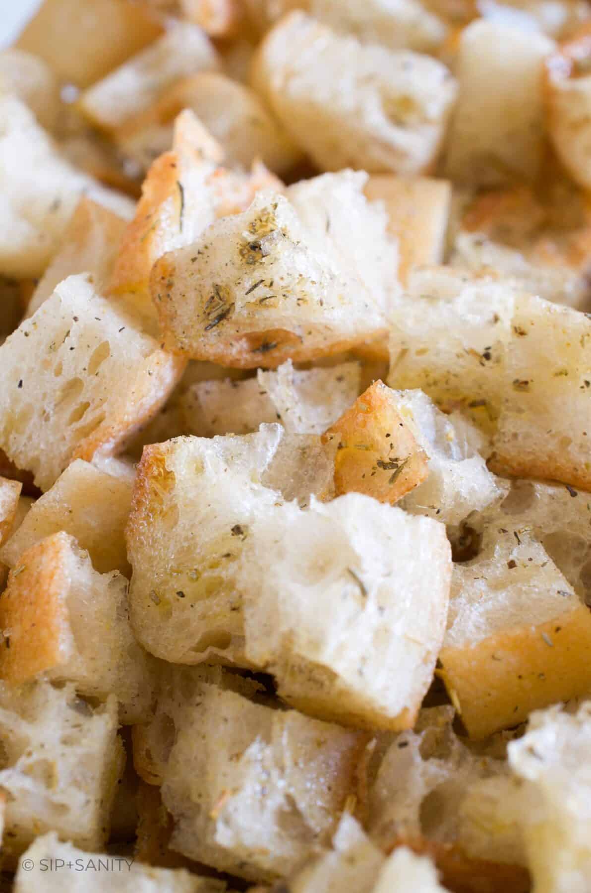 Close up of cubed bread pieces covered in olive oil and herb seasonings.