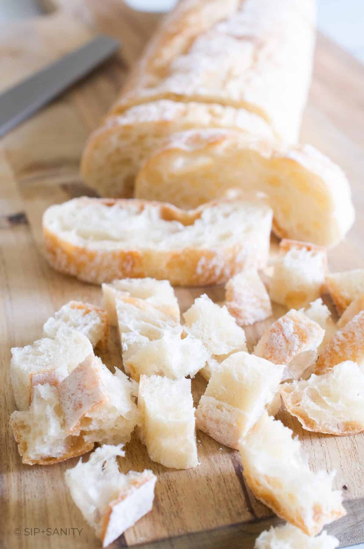 A baguette on a cutting board with slices and cubes of bread.