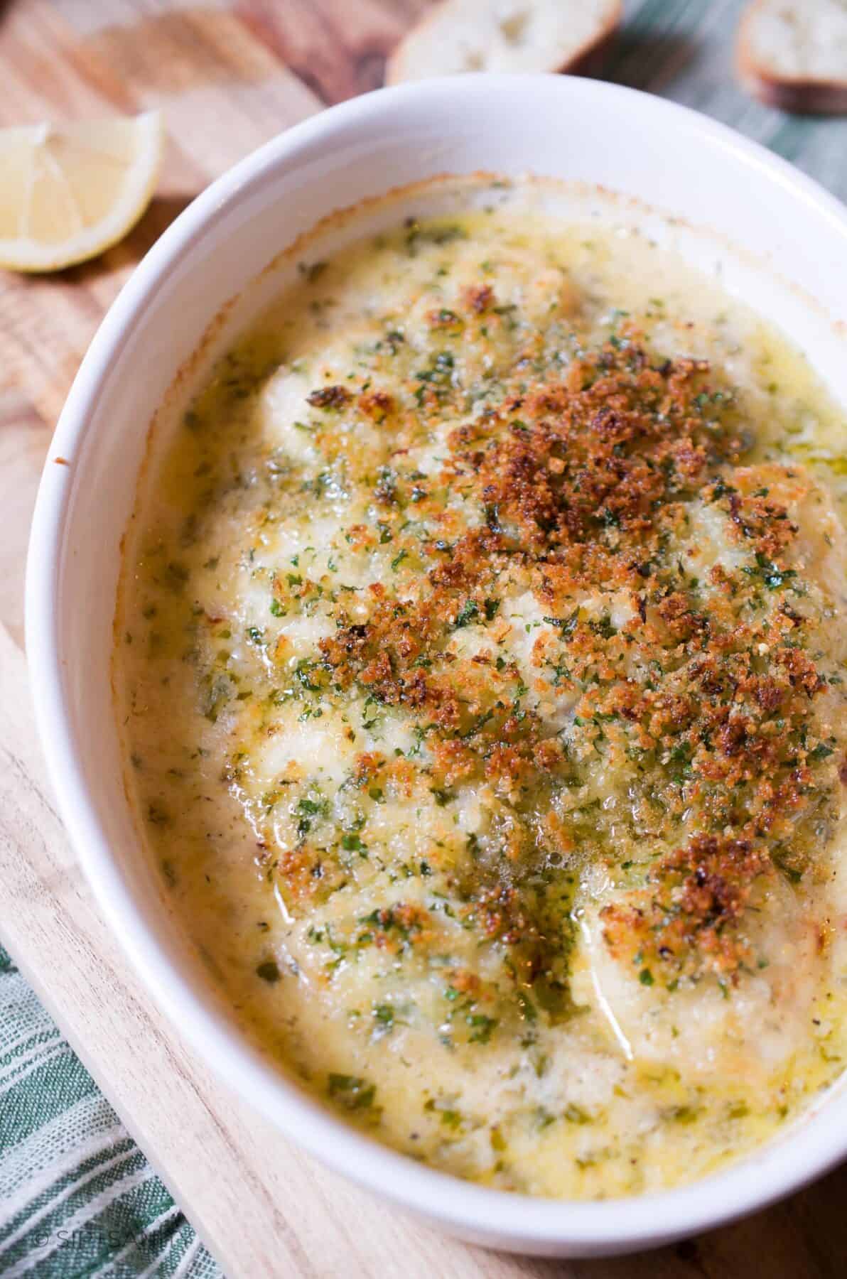 Breadcrumb topped baked scallops in white cream sauce in an oval baking dish.