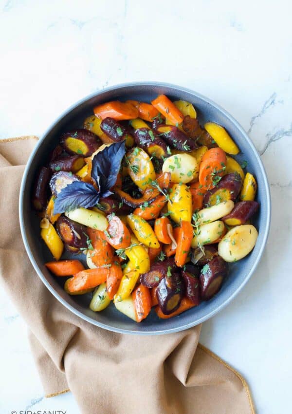 A round bowl filled with sliced roasted rainbow carrots on a white marble table.