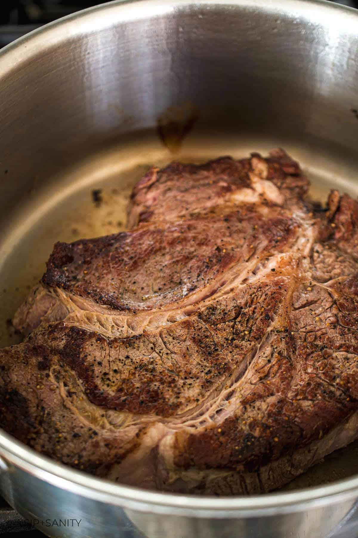 A chuck roast being seared in a stainless steel pot.