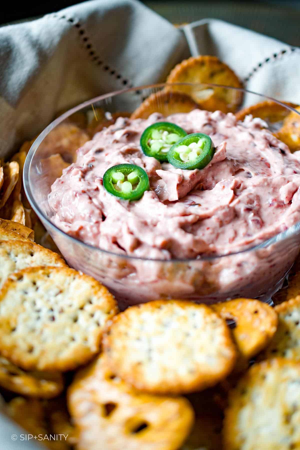 A glass bowl of cranberry cheese dip in a basket surrounded by crackers.