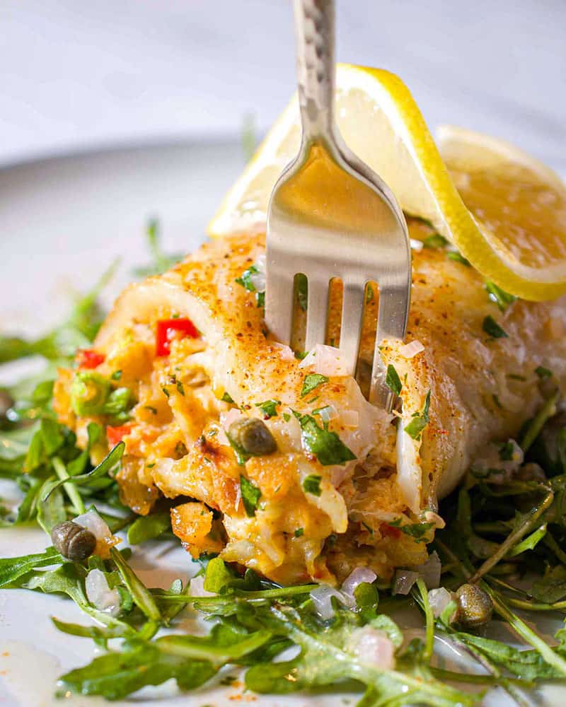 A fork spearing a crab stuffed flounder roulade on a bed of arugula.