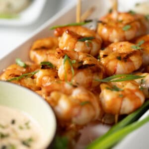 Several shrimp skewers arranged on a plate with sliced scallions.