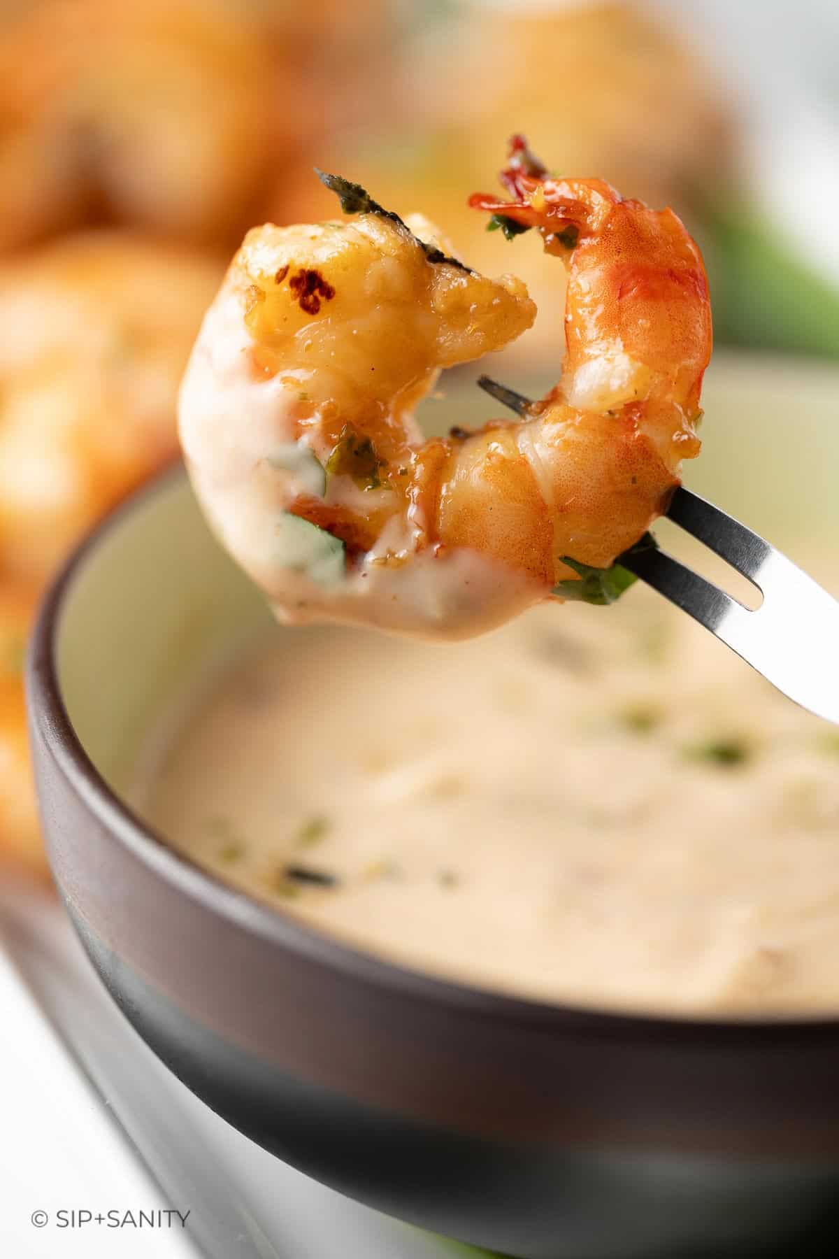 A grilled firecracker shrimp dripping with sauce on the end of a fork.